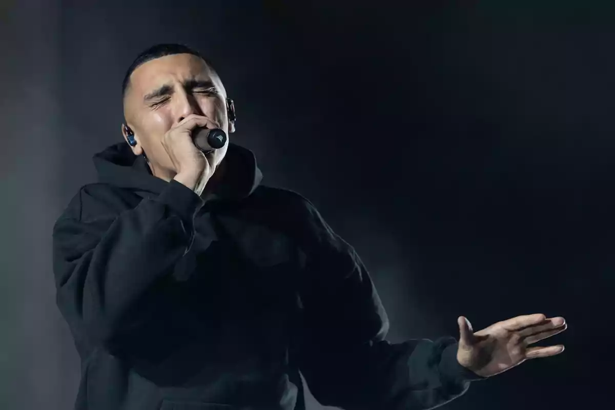 Hombre cantando apasionadamente en el escenario con sudadera negra y micrófono en mano