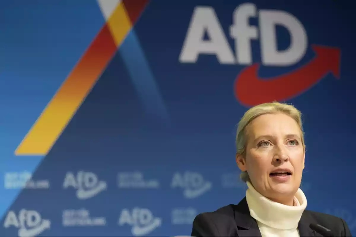 Mujer rubia hablando frente a un micrófono con fondo azul y logotipo de AfD Mujer rubia hablando frente a un micrófono con fondo azul y logotipo de AfD