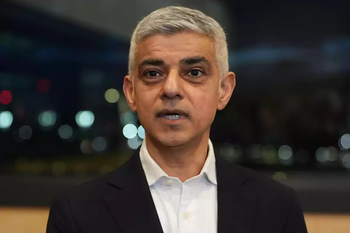 Hombre de cabello canoso y corto vistiendo camisa blanca y saco oscuro con fondo desenfocado de luces nocturnas