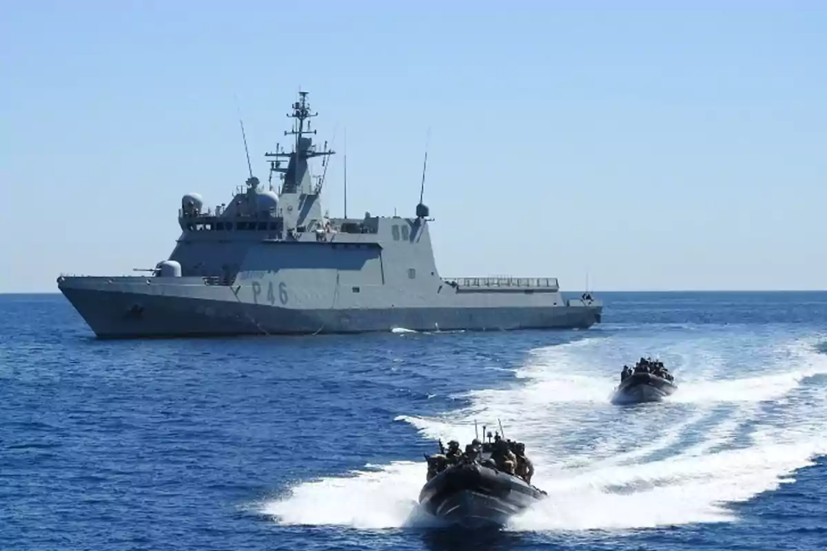 Un buque militar gris navega en el mar acompañado por dos lanchas rápidas con personal a bordo Un buque militar gris navega en el mar acompañado por dos lanchas rápidas con personal a bordo