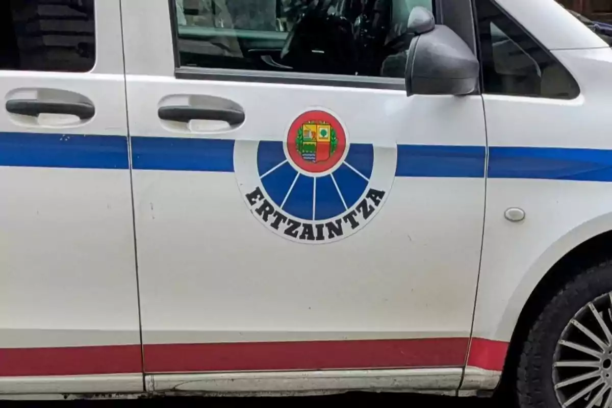 Puerta de una furgoneta blanca con una franja azul y roja y el escudo de la Ertzaintza
