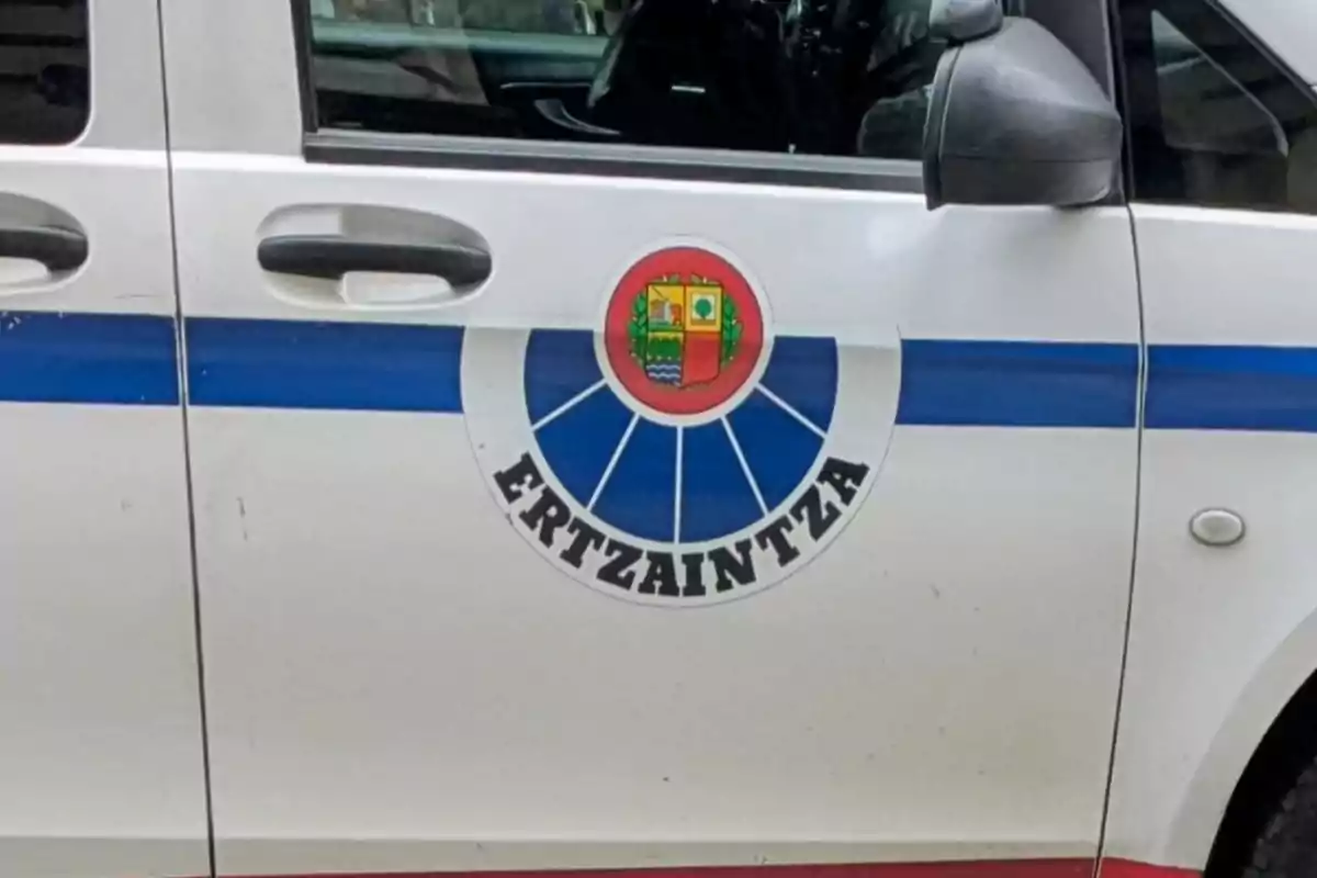 Puerta de un coche policial blanco con una franja azul y el escudo de la Ertzaintza Puerta de un coche policial blanco con una franja azul y el escudo de la Ertzaintza