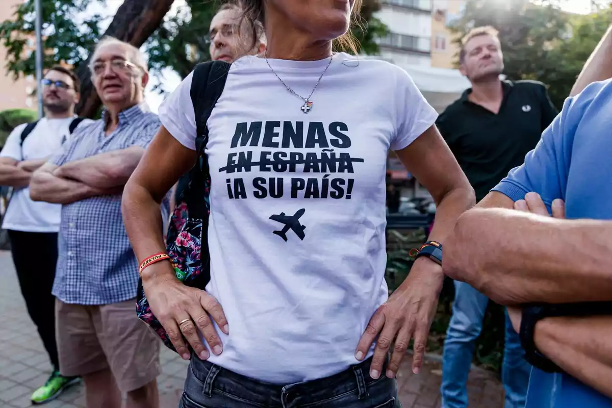Mujer con camiseta blanca con mensaje en contra de los menores extranjeros no acompañados rodeada de varias personas en la calle Mujer con camiseta blanca con mensaje en contra de los menores extranjeros no acompañados rodeada de varias personas en la calle
