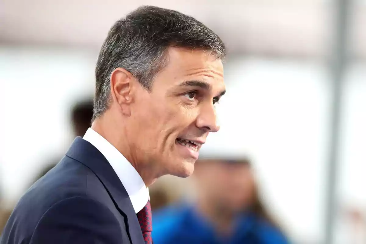 Hombre de cabello corto y canoso vistiendo traje oscuro y corbata roja hablando en un entorno profesional Hombre de cabello corto y canoso vistiendo traje oscuro y corbata roja hablando en un entorno profesional