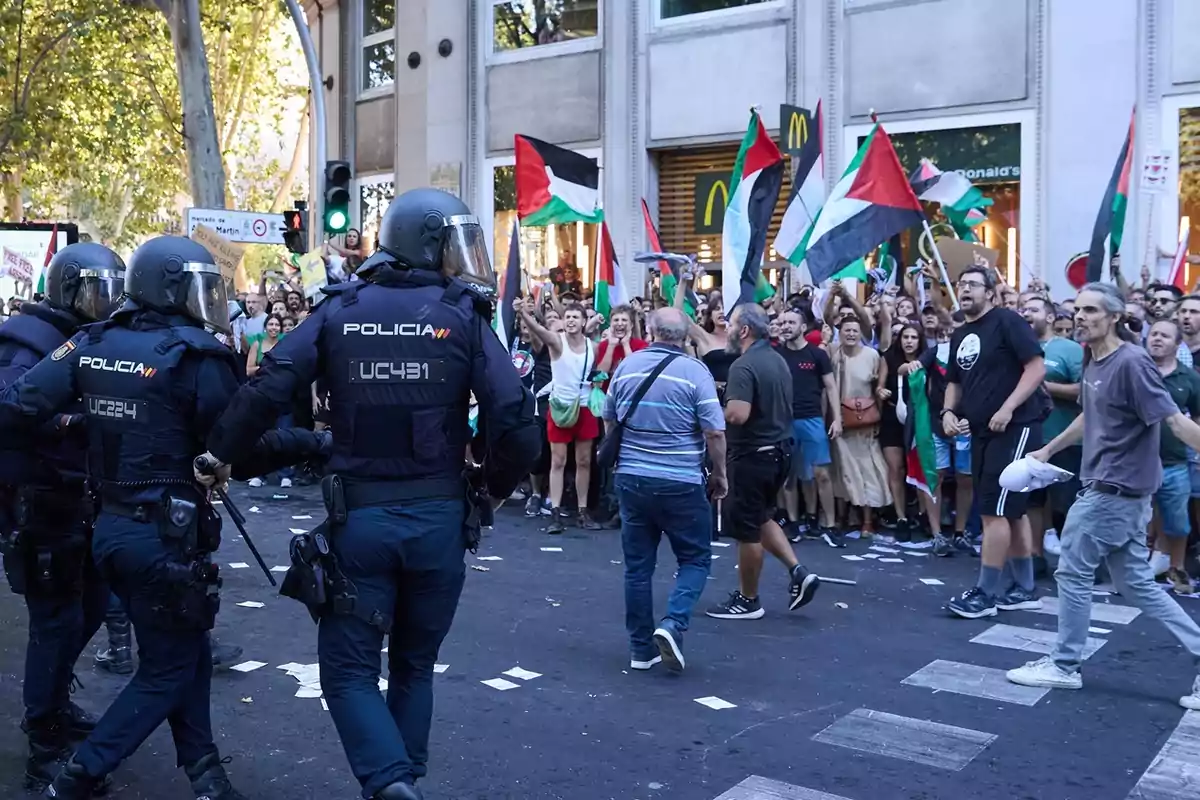Policías antidisturbios observan a un grupo de manifestantes que ondean banderas palestinas frente a un restaurante de comida rápida en una ciudad