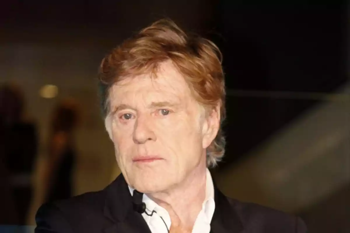 Hombre de cabello rubio y expresión seria vistiendo saco oscuro y camisa blanca