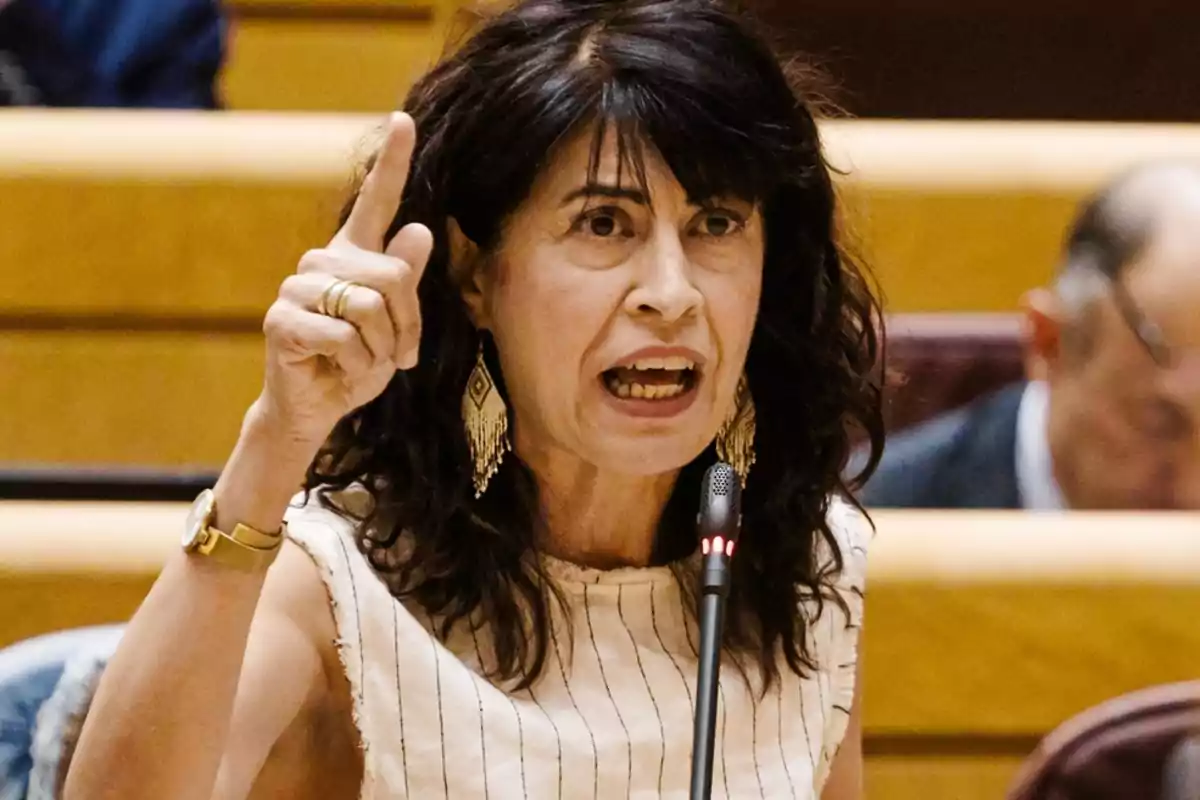 Mujer de cabello oscuro hablando apasionadamente en un micrófono mientras levanta el dedo índice en un entorno formal