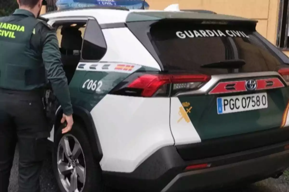 Agente de la Guardia Civil junto a un coche patrulla con la puerta trasera abierta Agente de la Guardia Civil junto a un coche patrulla con la puerta trasera abierta
