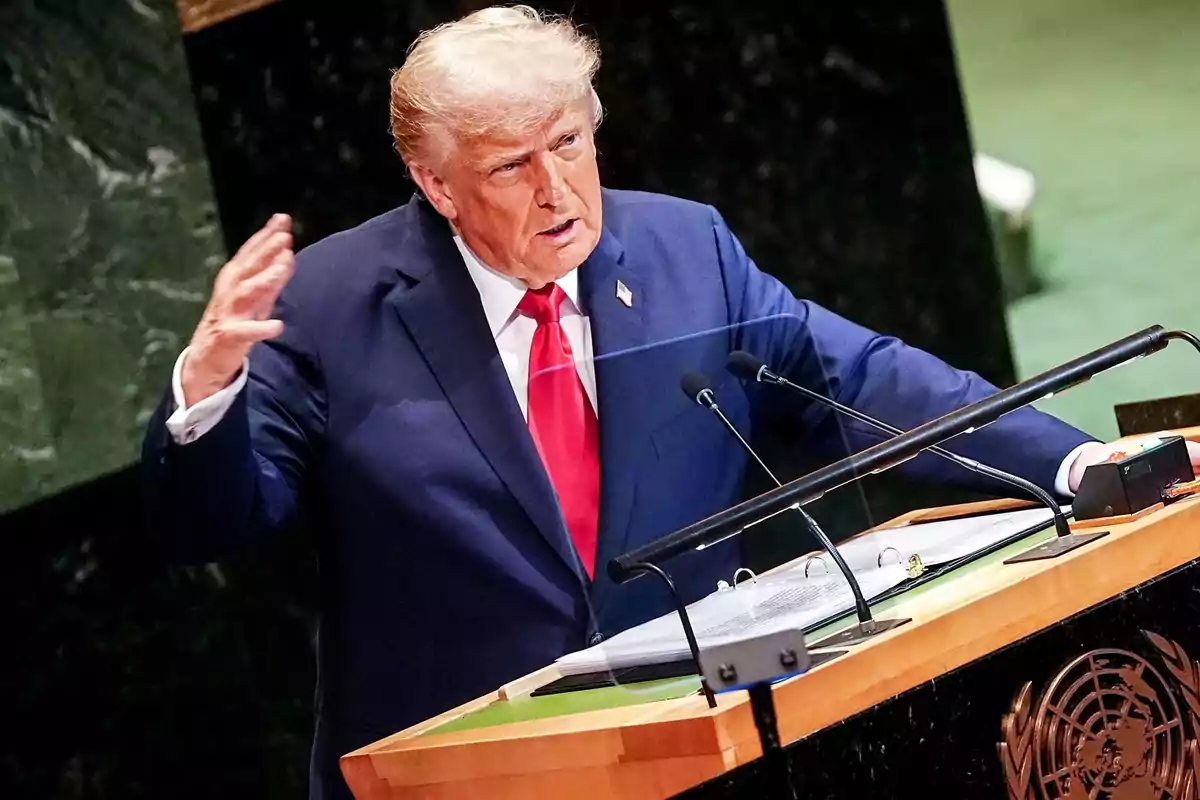 Hombre de cabello rubio con traje azul y corbata roja hablando en un podio con el emblema de la ONU Hombre de cabello rubio con traje azul y corbata roja hablando en un podio con el emblema de la ONU