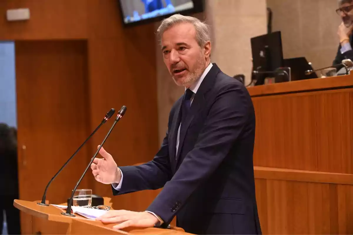 Hombre de cabello canoso y barba hablando en un podio con micrófonos en un entorno formal