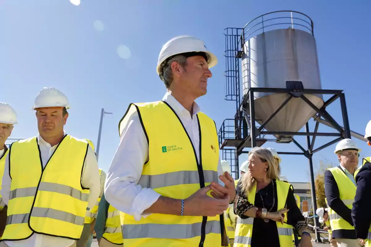 Grupo de personas con chalecos reflectantes y cascos de seguridad en una visita a una obra industrial bajo un cielo despejado