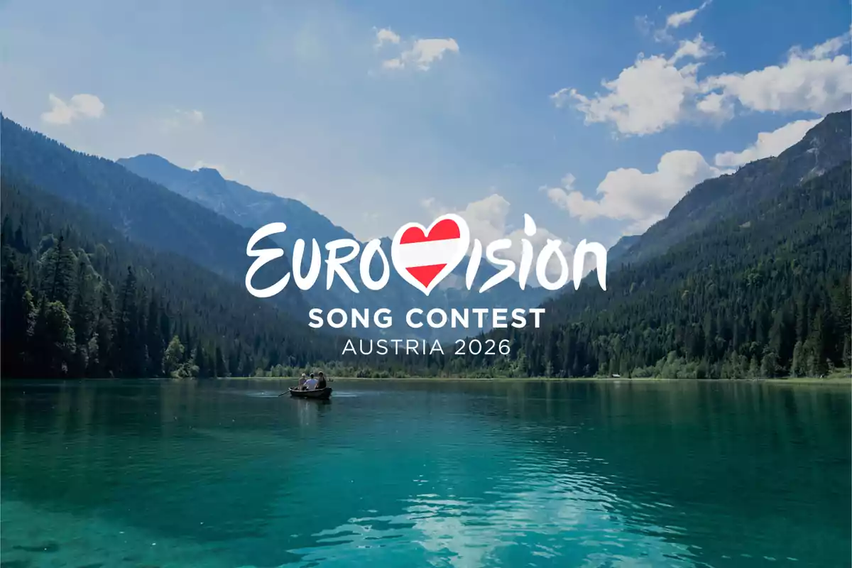 Logo de Eurovision Song Contest Austria 2026 sobre un lago rodeado de montañas y bosque bajo un cielo azul con nubes Logo de Eurovision Song Contest Austria 2026 sobre un lago rodeado de montañas y bosque bajo un cielo azul con nubes