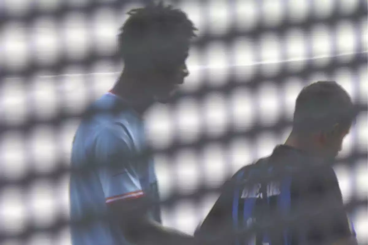 Dos jugadores de fútbol vistos a través de una malla desenfocada uno con camiseta clara y otro con camiseta oscura Dos jugadores de fútbol vistos a través de una malla desenfocada uno con camiseta clara y otro con camiseta oscura