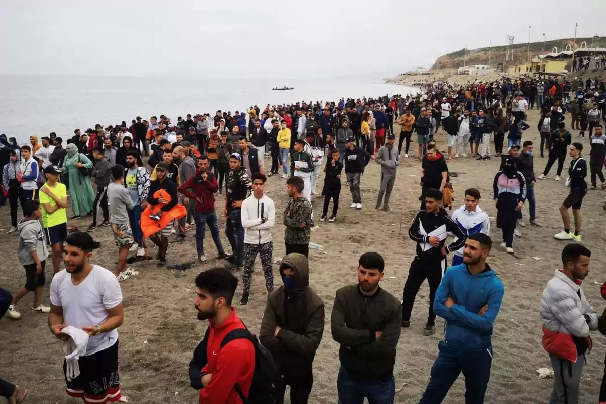 Multitud de personas reunidas en una playa mirando hacia diferentes direcciones en un día nublado