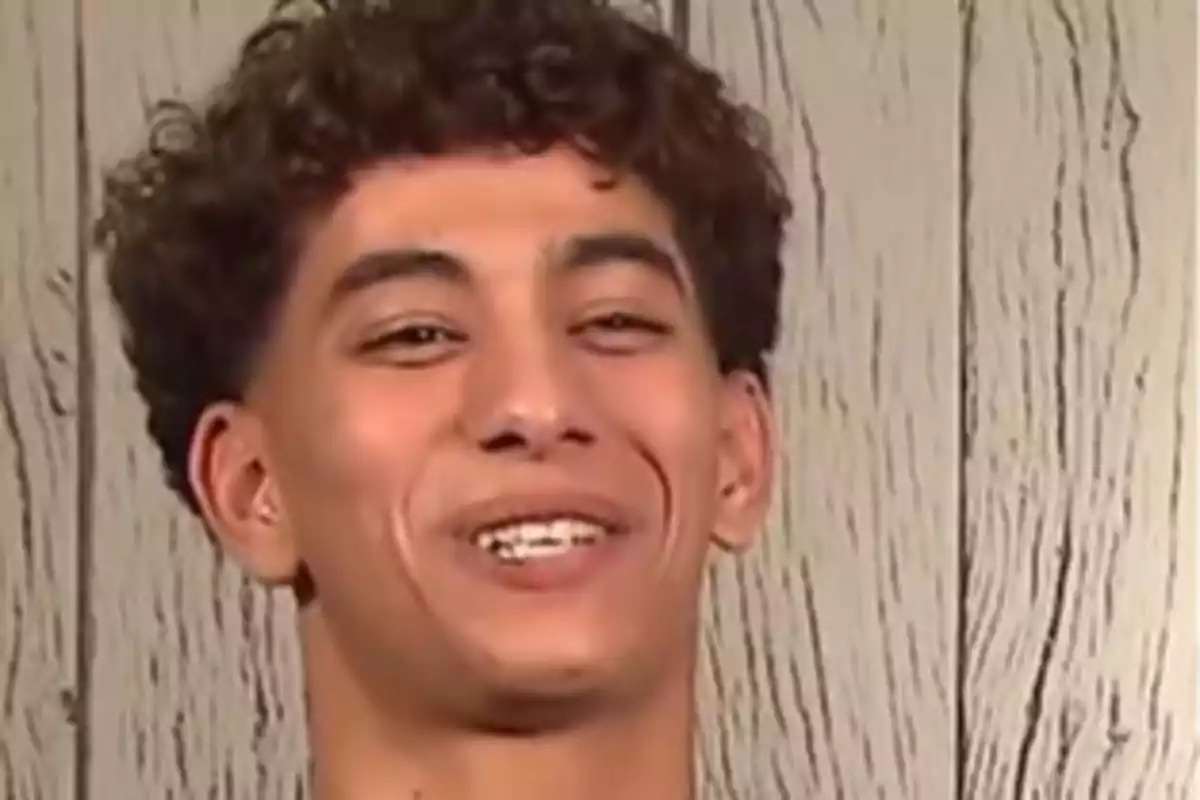 Joven de cabello rizado sonriendo frente a una pared de madera clara Joven de cabello rizado sonriendo frente a una pared de madera clara