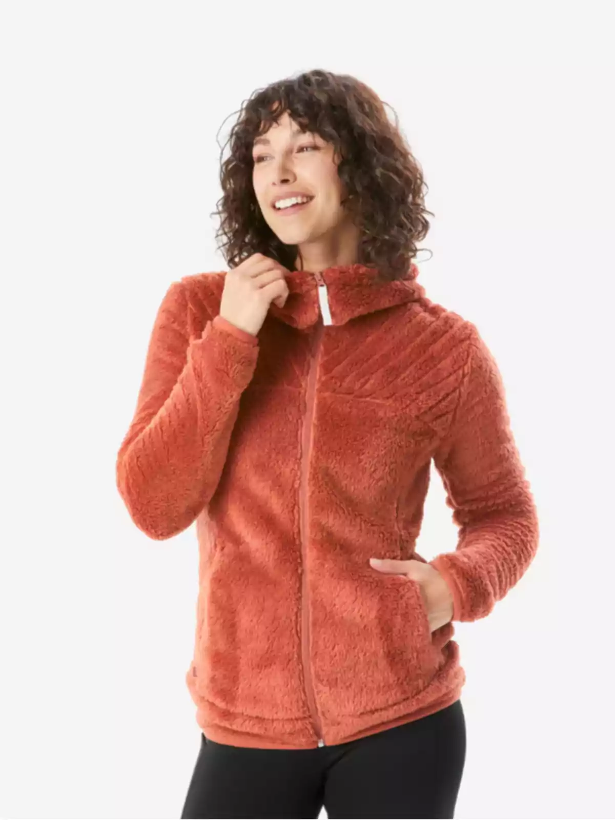 Mujer sonriente con chaqueta de felpa color terracota y pantalones oscuros sobre fondo claro Mujer sonriente con chaqueta de felpa color terracota y pantalones oscuros sobre fondo claro