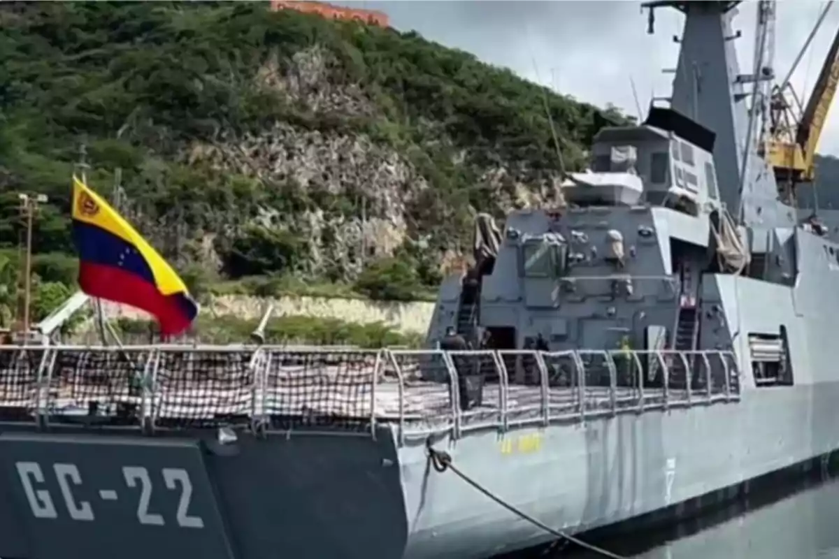 Buque militar gris con la bandera de Venezuela atracado junto a una colina cubierta de vegetación Buque militar gris con la bandera de Venezuela atracado junto a una colina cubierta de vegetación