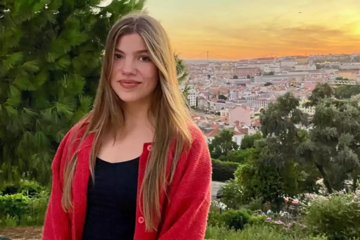 La infanta Sofía con cabello largo y suelto, usando un suéter rojo y camiseta negra, posando en un mirador con vista a una ciudad al atardecer La infanta Sofía con cabello largo y suelto, usando un suéter rojo y camiseta negra, posando en un mirador con vista a una ciudad al atardecer