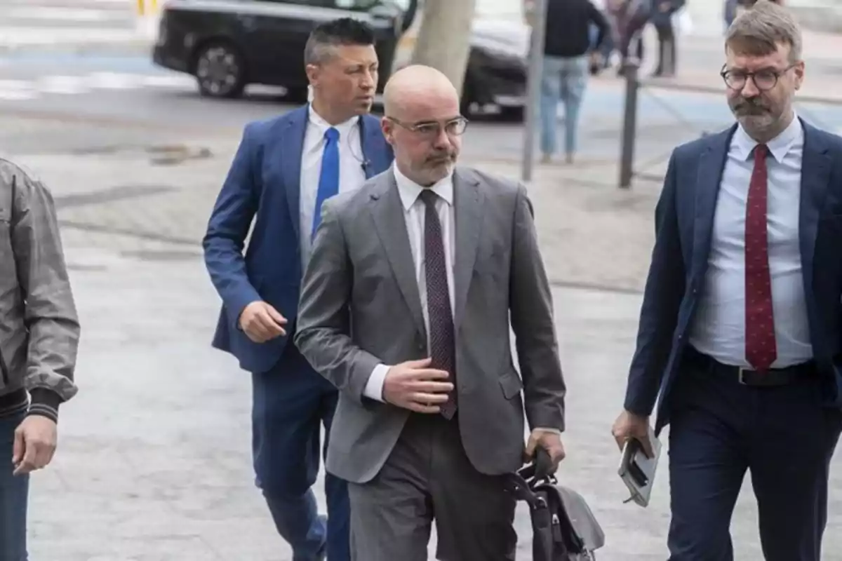 Tres hombres con traje caminan por la calle en un entorno urbano, uno de ellos lleva una carpeta y otro una bolsa de mano. Tres hombres con traje caminan por la calle en un entorno urbano, uno de ellos lleva una carpeta y otro una bolsa de mano.