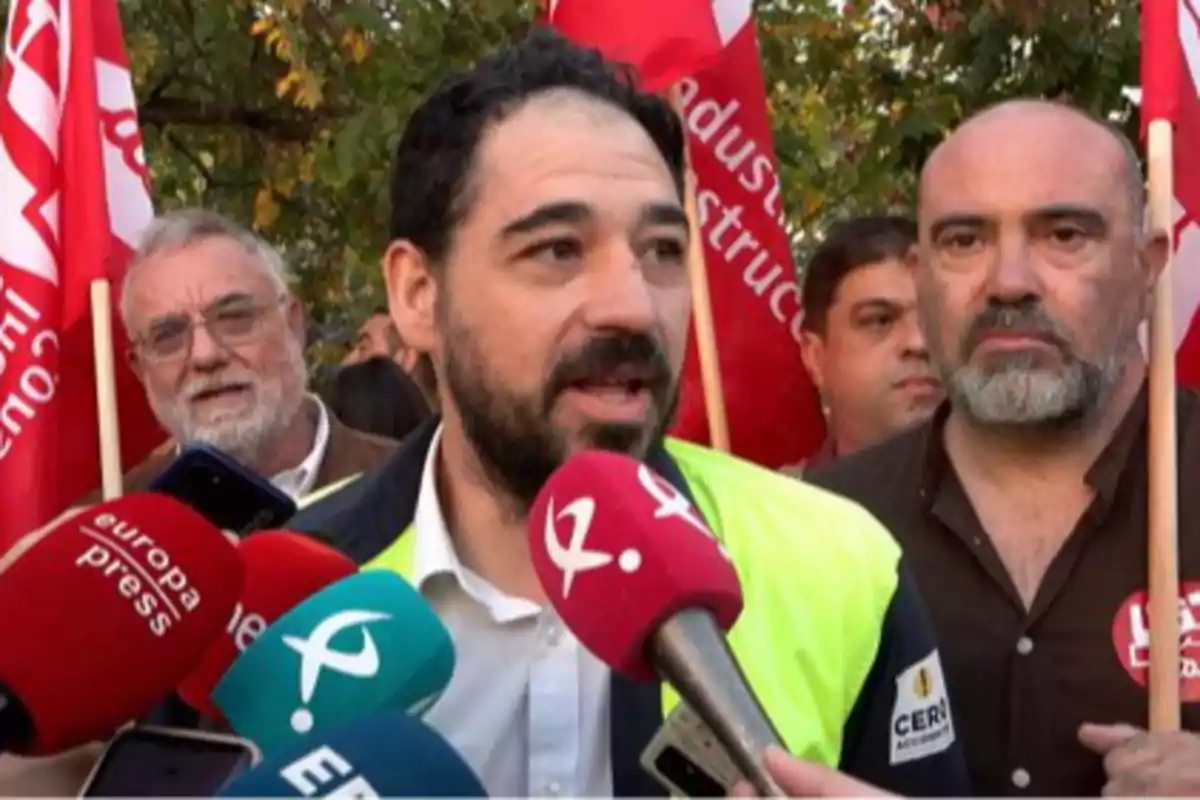 Un hombre con chaleco amarillo habla ante varios micrófonos de prensa rodeado de personas con banderas rojas en una manifestación Un hombre con chaleco amarillo habla ante varios micrófonos de prensa rodeado de personas con banderas rojas en una manifestación
