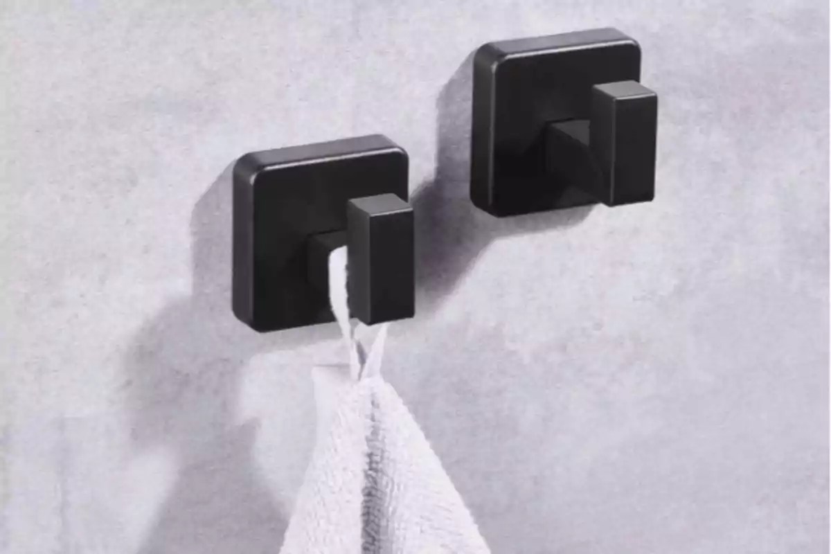 Dos ganchos cuadrados negros en la pared sosteniendo una toalla blanca Dos ganchos cuadrados negros en la pared sosteniendo una toalla blanca