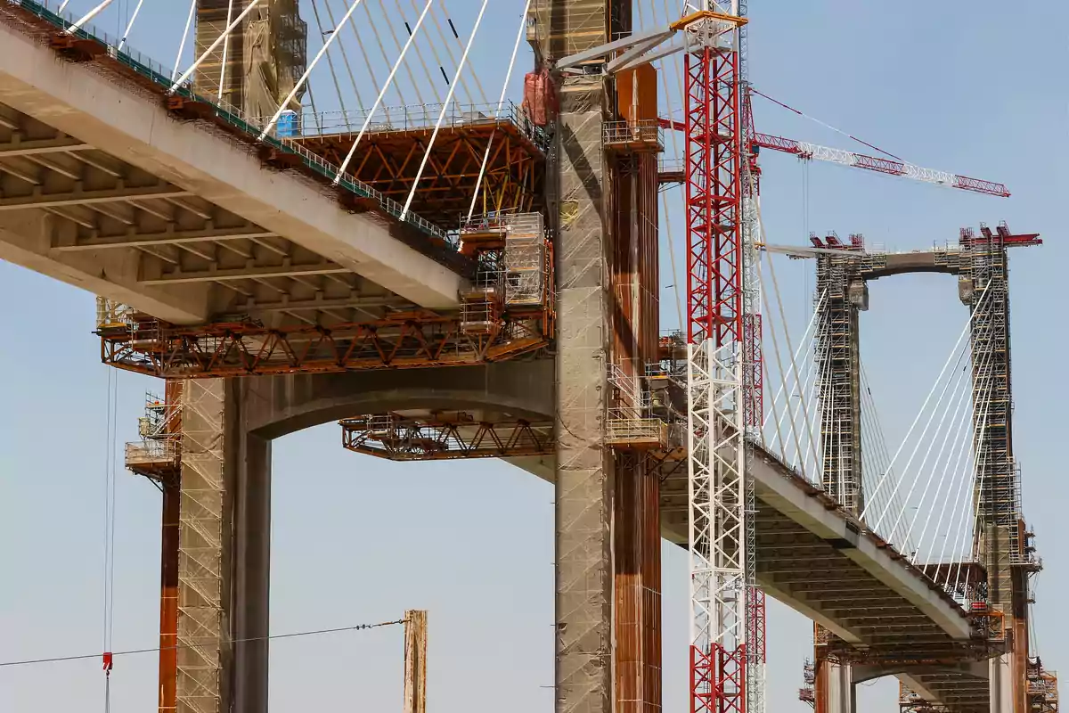 Puente atirantado en construcción con grúas y estructuras de soporte visibles Puente atirantado en construcción con grúas y estructuras de soporte visibles