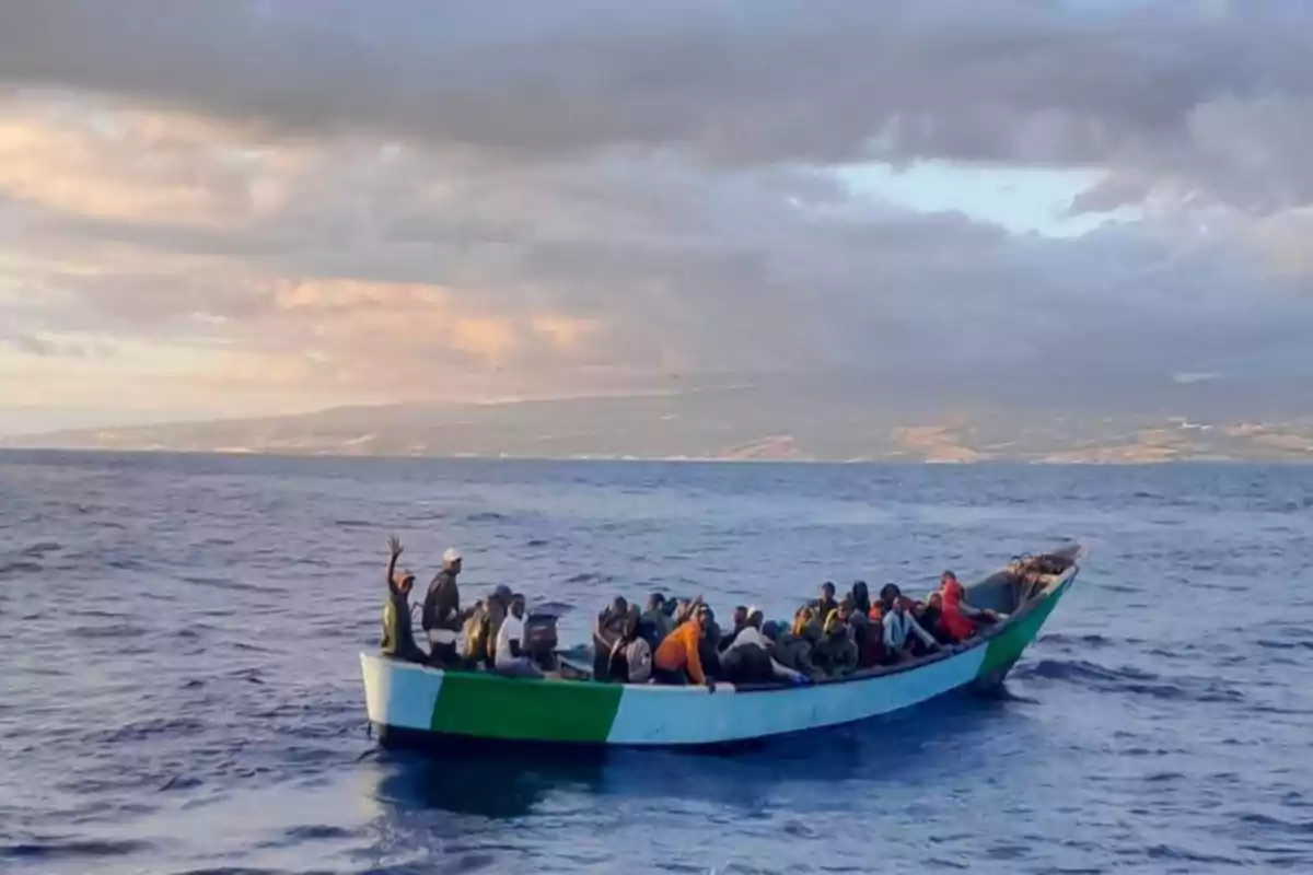 Un grupo de personas viaja en una pequeña embarcación sobre el mar bajo un cielo nublado con montañas al fondo Un grupo de personas viaja en una pequeña embarcación sobre el mar bajo un cielo nublado con montañas al fondo