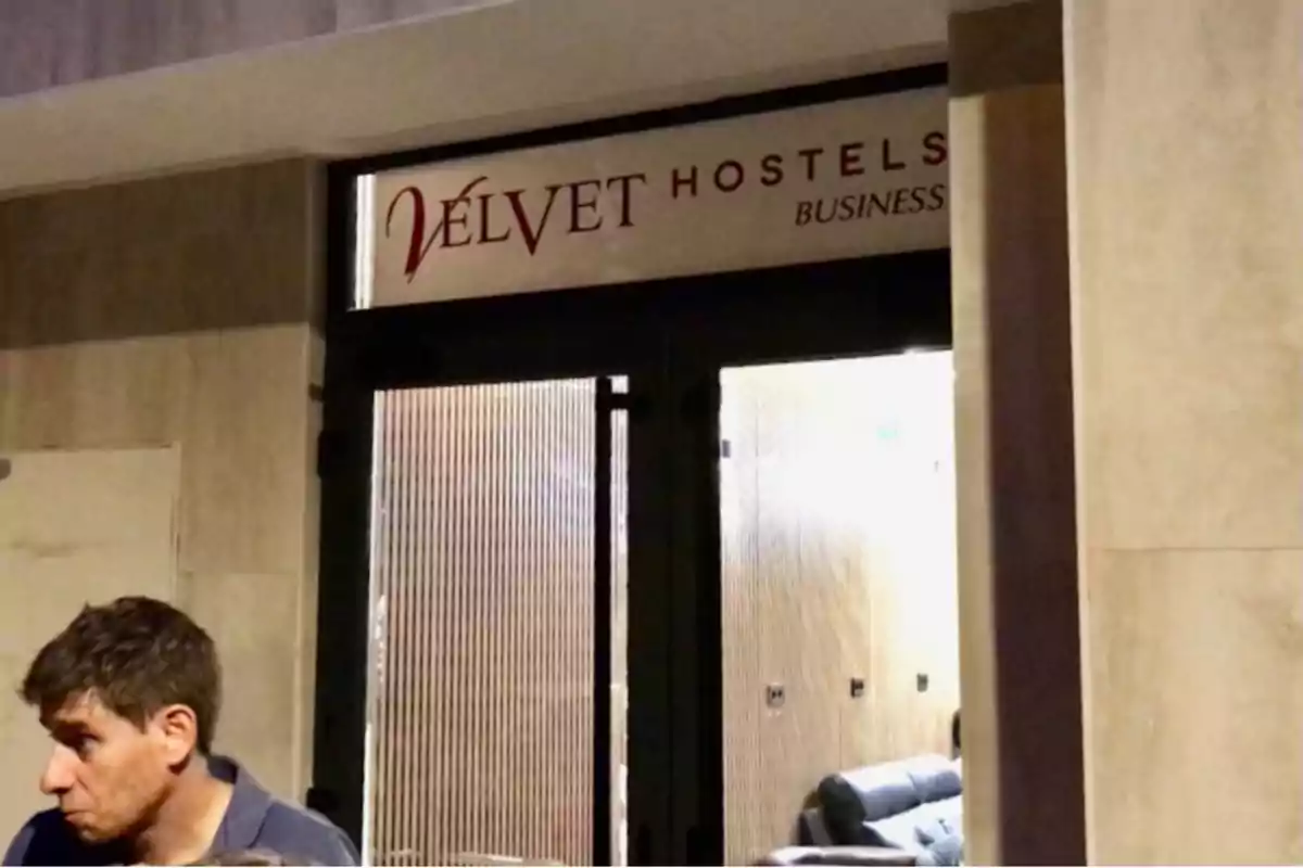 Entrada de un hostal llamado Velvet Hostels Business con una persona de cabello corto en primer plano a la izquierda