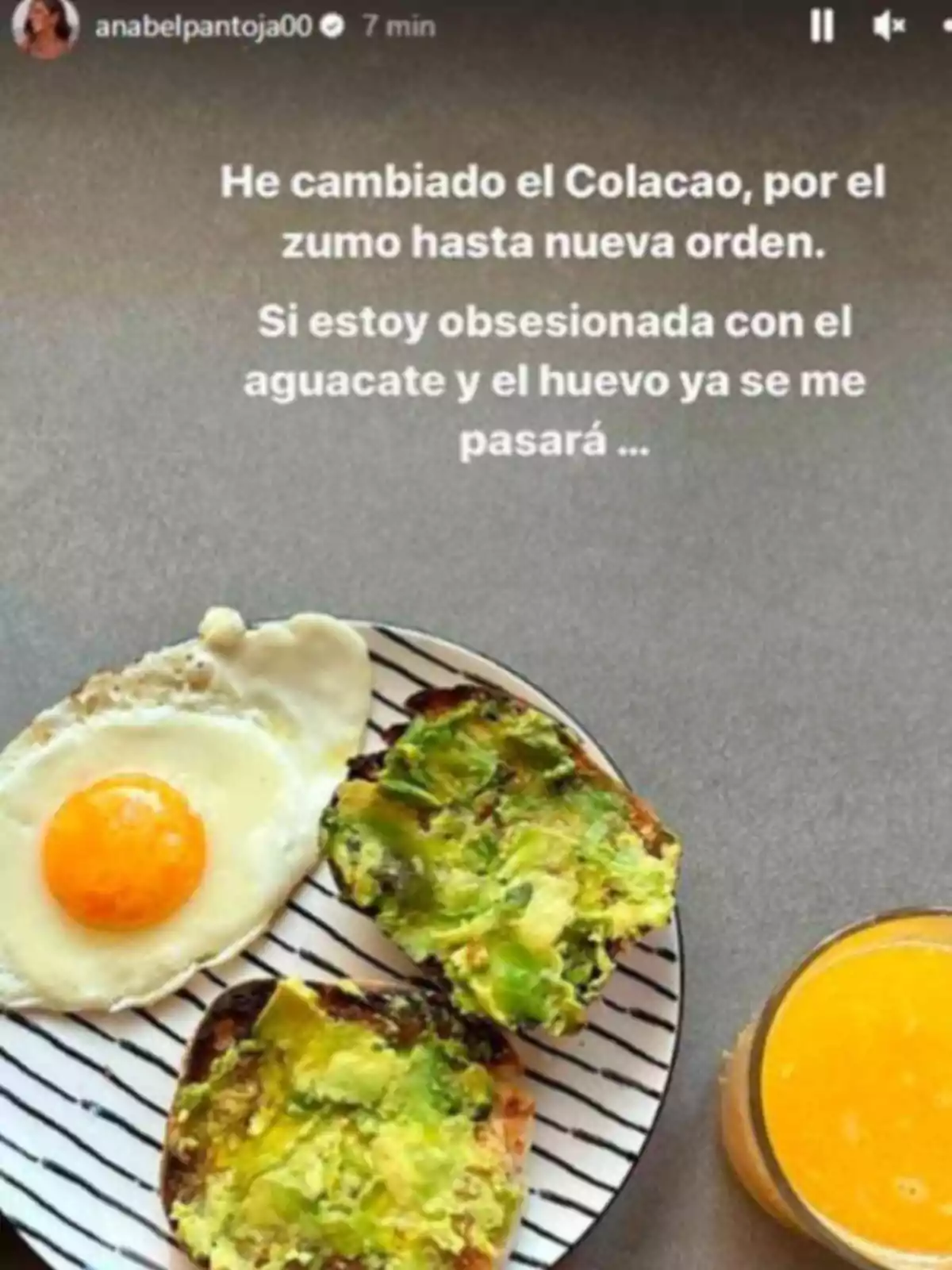 Desayuno con huevo frito, pan con aguacate y un vaso de zumo de naranja sobre una mesa gris Desayuno con huevo frito, pan con aguacate y un vaso de zumo de naranja sobre una mesa gris