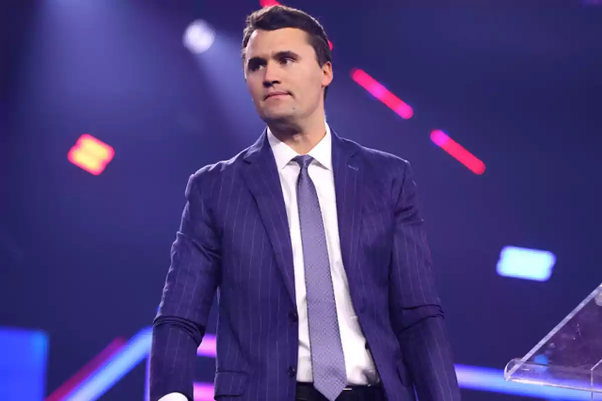 Hombre de traje azul con corbata de pie en un escenario iluminado con luces de colores en el fondo