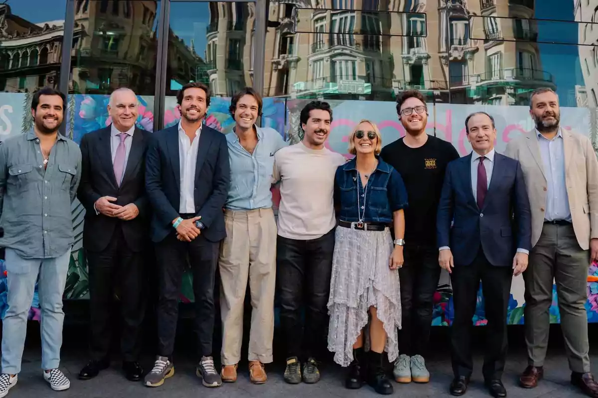 Grupo de personas posando sonrientes frente a un edificio con ventanas de cristal y un mural colorido de fondo