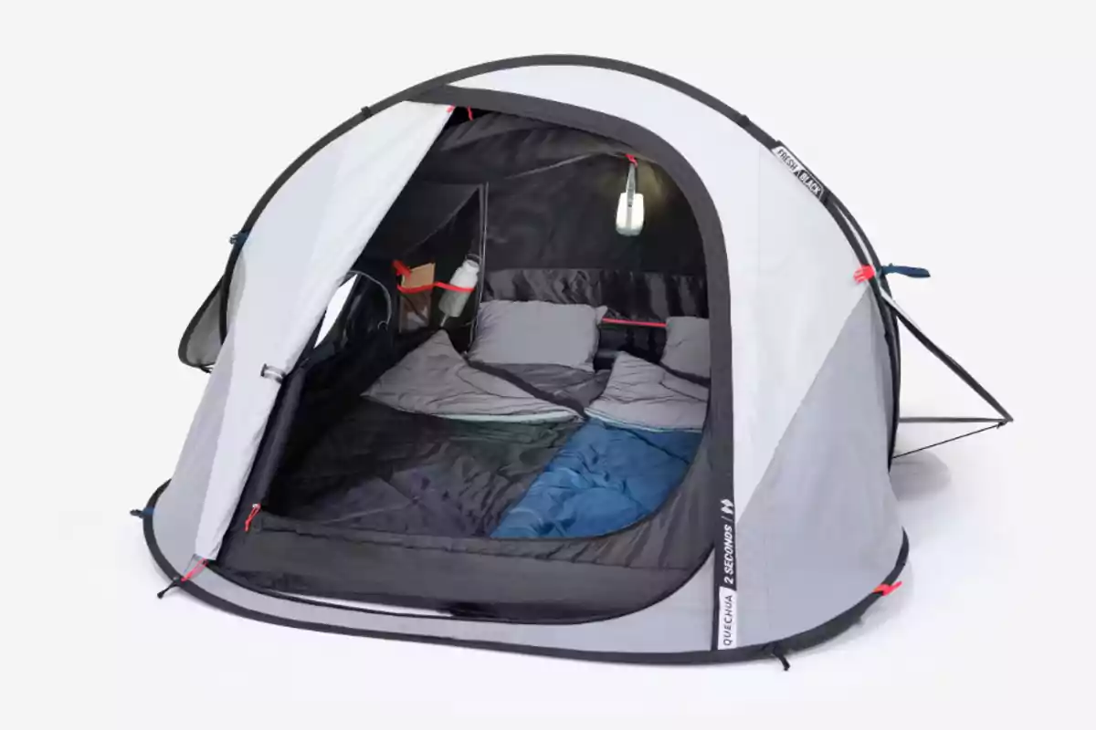 Tienda de campaña gris armada con la entrada abierta mostrando dos sacos de dormir y almohadas en su interior