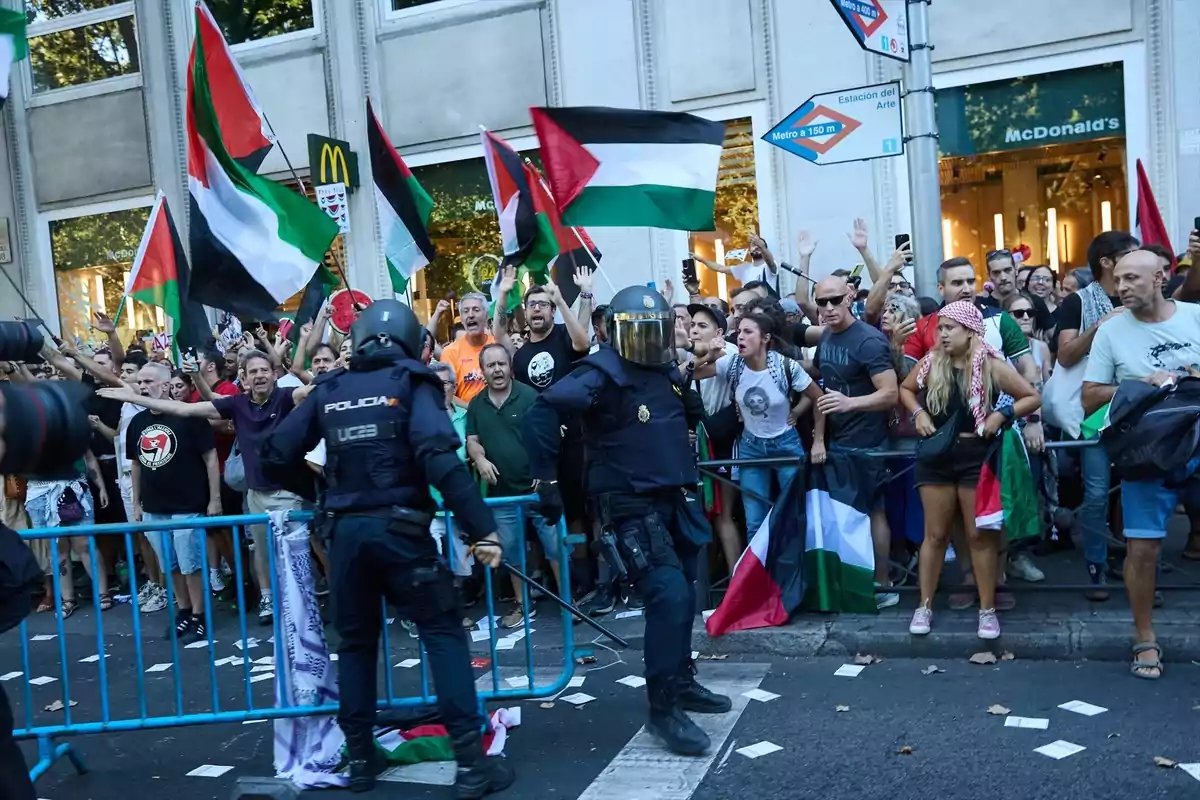 Manifestantes con banderas palestinas protestan frente a un cordón policial en una calle urbana