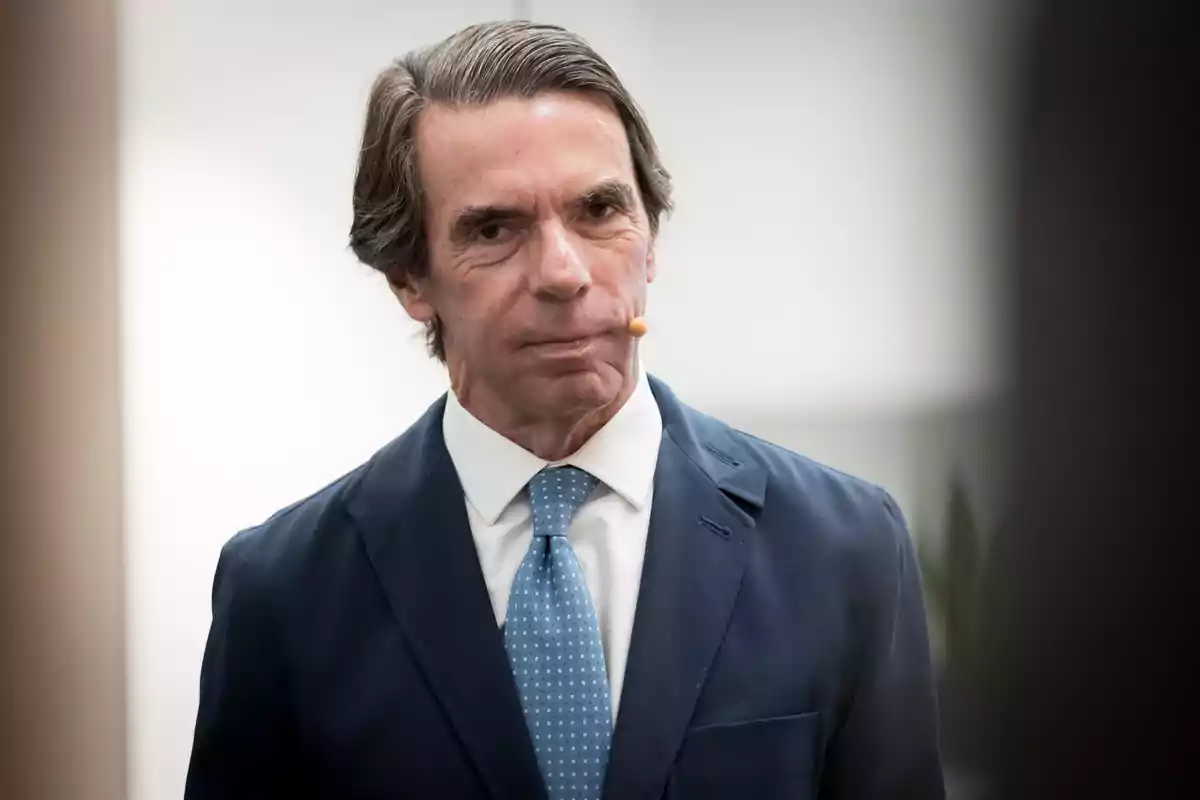 José María Aznar con traje azul y corbata celeste usando un micrófono de diadema