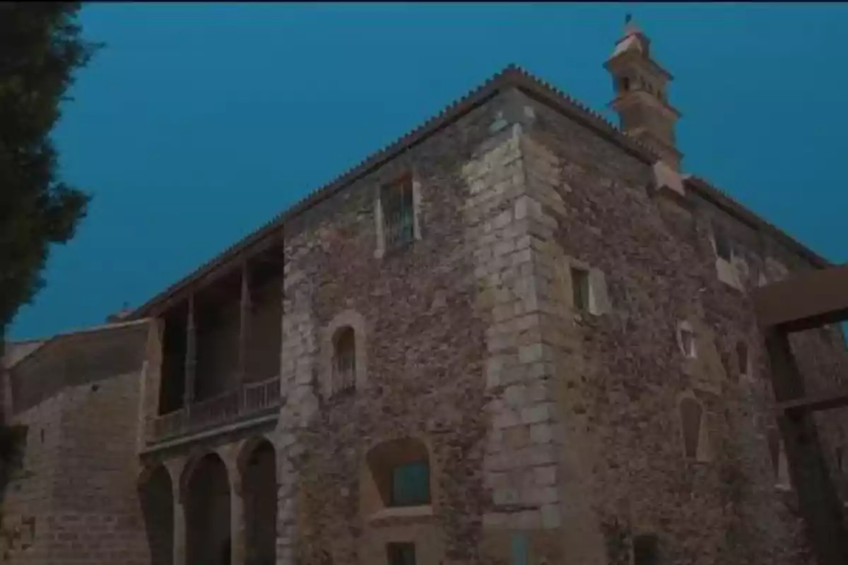 Edificio antiguo de piedra con arcos y una torre bajo un cielo azul