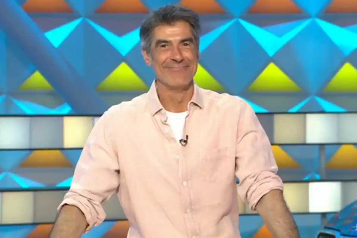 Jorge Fernández con camisa clara sonríe frente a un fondo colorido con figuras geométricas. Captura de 'La Ruleta de la Suerte'