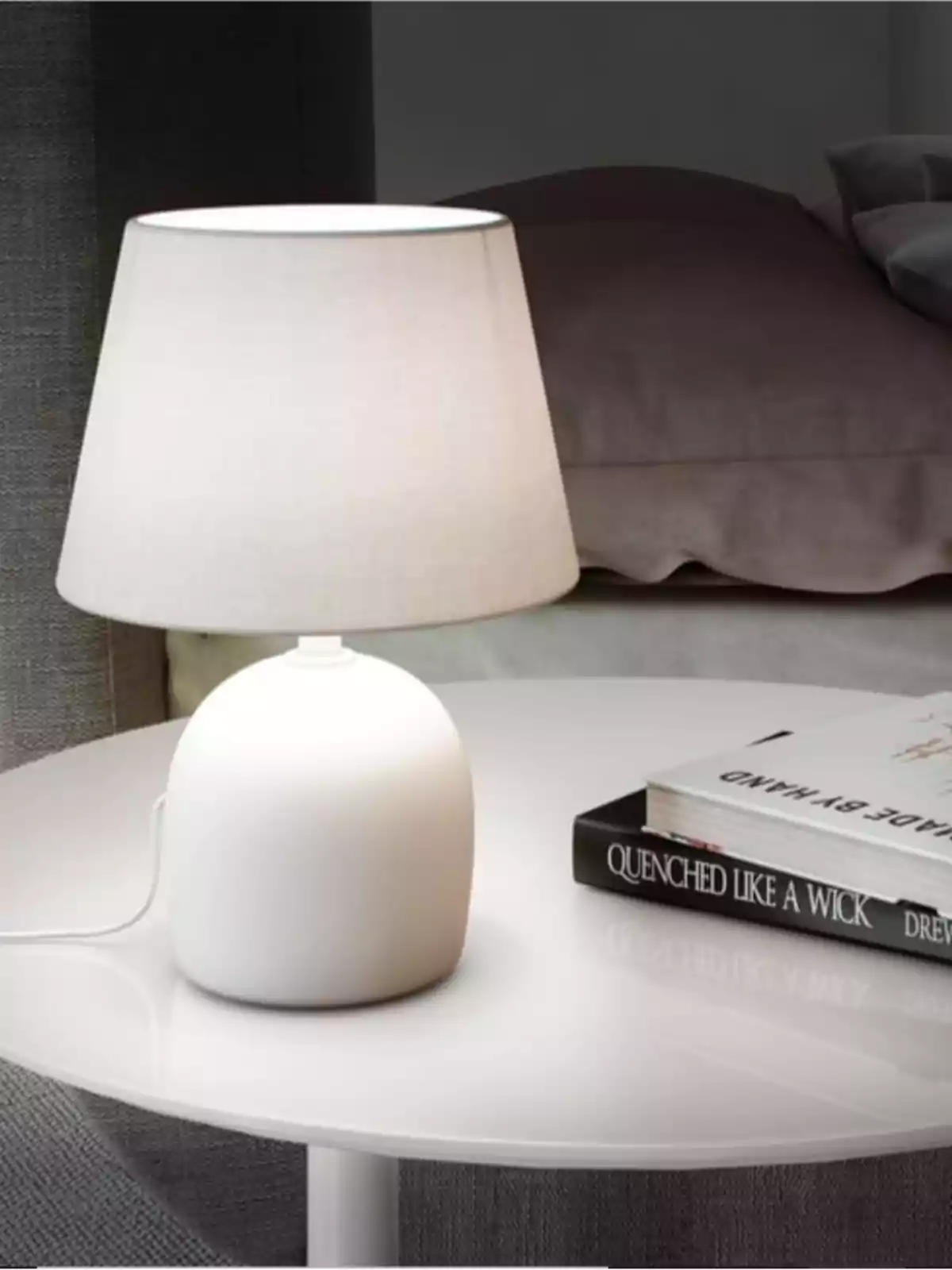 Lámpara de mesa blanca encendida sobre una mesa redonda junto a un par de libros en una habitación acogedora Lámpara de mesa blanca encendida sobre una mesa redonda junto a un par de libros en una habitación acogedora
