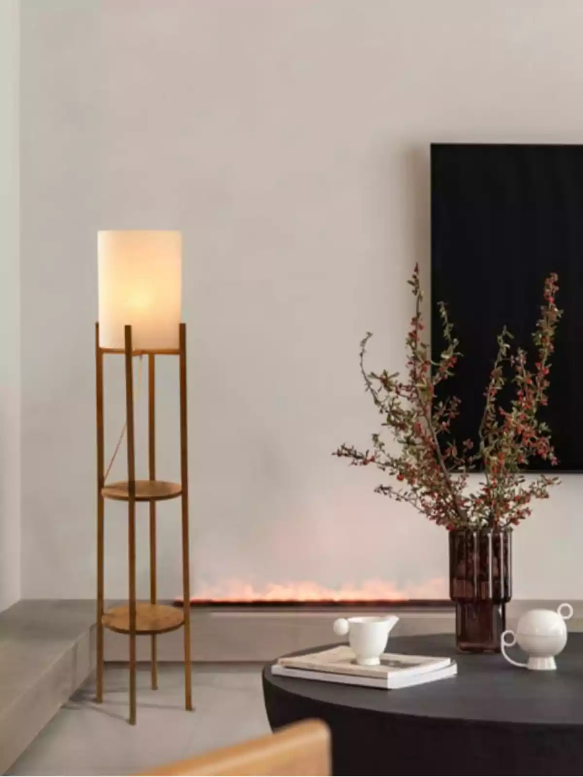 Sala moderna con lámpara de pie encendida, mesa negra con jarrón de flores y tazas blancas, fondo con chimenea y televisor en la pared Sala moderna con lámpara de pie encendida, mesa negra con jarrón de flores y tazas blancas, fondo con chimenea y televisor en la pared