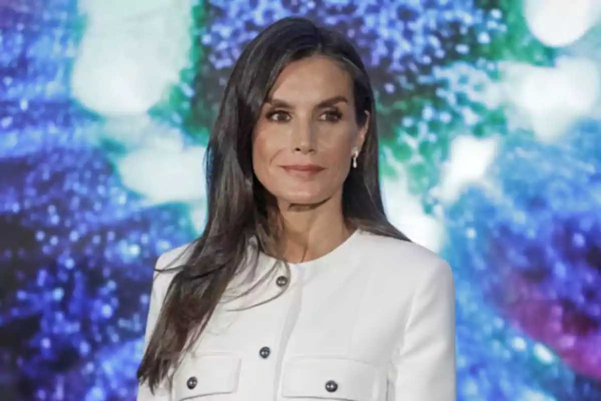 Letizia Ortiz de cabello largo y oscuro con chaqueta blanca posando frente a un fondo colorido desenfocado
