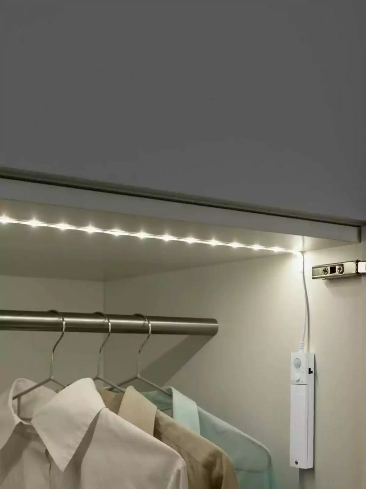 Ropa colgada en un armario iluminado con una tira de luces LED y un sensor en la pared. Ropa colgada en un armario iluminado con una tira de luces LED y un sensor en la pared.