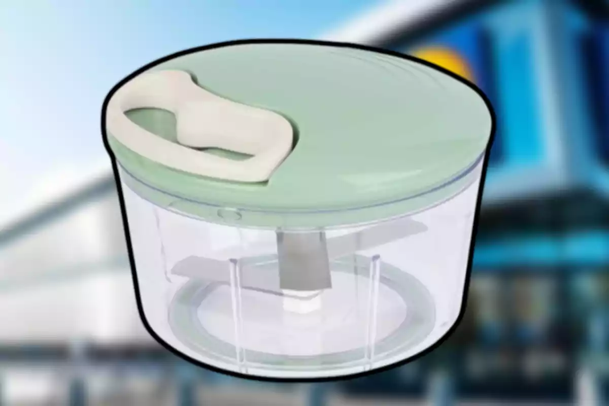 Recipiente transparente con tapa verde y manija blanca, diseñado para picar alimentos manualmente, sobre un fondo desenfocado de edificio moderno. Recipiente transparente con tapa verde y manija blanca, diseñado para picar alimentos manualmente, sobre un fondo desenfocado de edificio moderno.