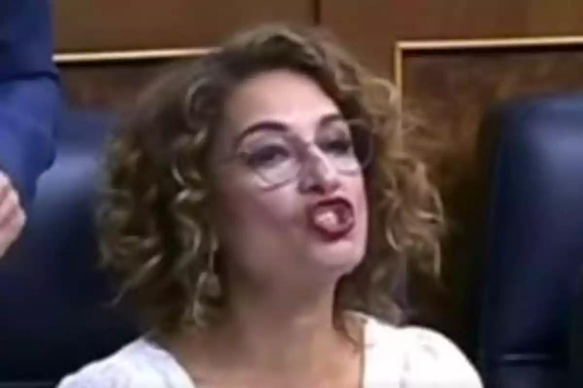 Mujer de cabello rizado y gafas hablando con expresión enfática en un entorno formal