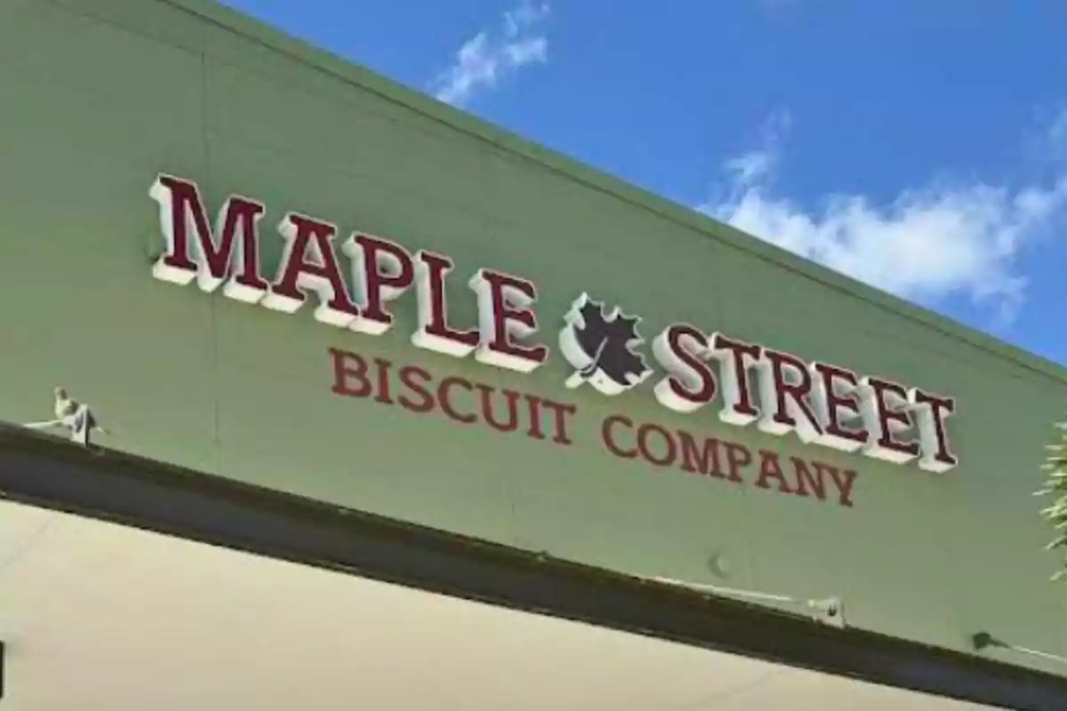 Letrero de la tienda Maple Street Biscuit Company sobre una pared verde bajo un cielo azul con algunas nubes