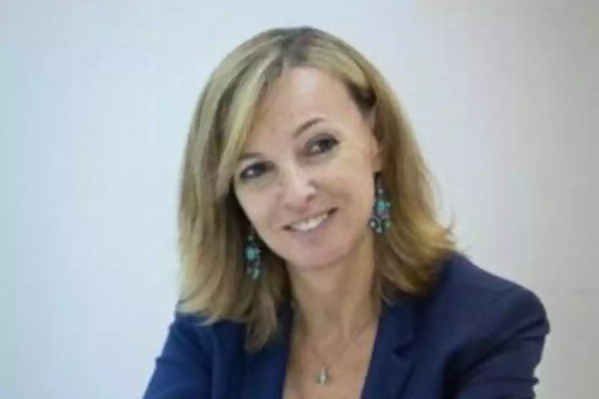 Mujer de cabello rubio y corto con chaqueta azul sonriendo y usando aretes largos turquesa Mujer de cabello rubio y corto con chaqueta azul sonriendo y usando aretes largos turquesa