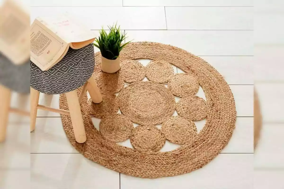 Un tapete redondo de fibras naturales con diseño de círculos de Leroy Merlin está sobre un piso claro junto a un banco de madera con asiento tapizado y un libro abierto, además de una maceta con planta verde.