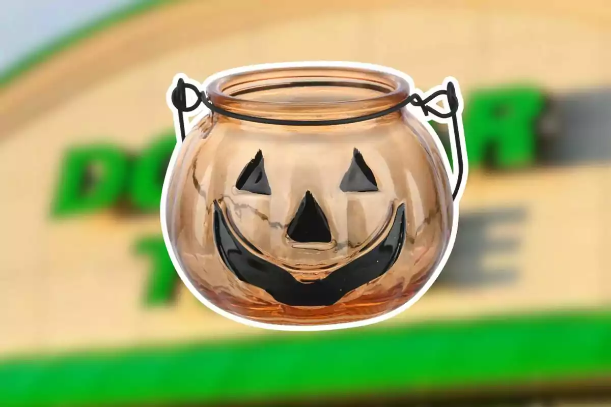 Calabaza de plástico transparente con cara sonriente de Halloween y asa negra sobre un fondo borroso de tienda.
