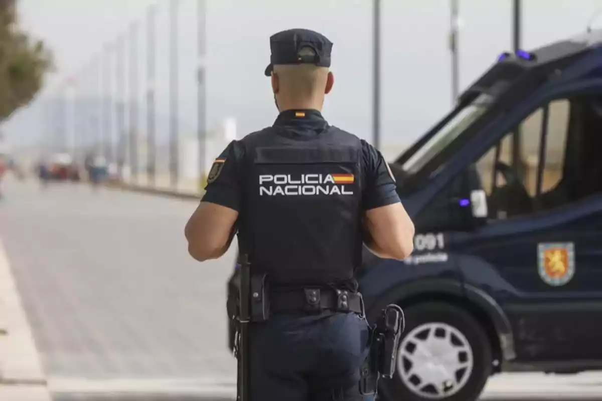 Agente de la Policía Nacional de España de espaldas patrullando junto a una furgoneta policial en la calle Agente de la Policía Nacional de España de espaldas patrullando junto a una furgoneta policial en la calle
