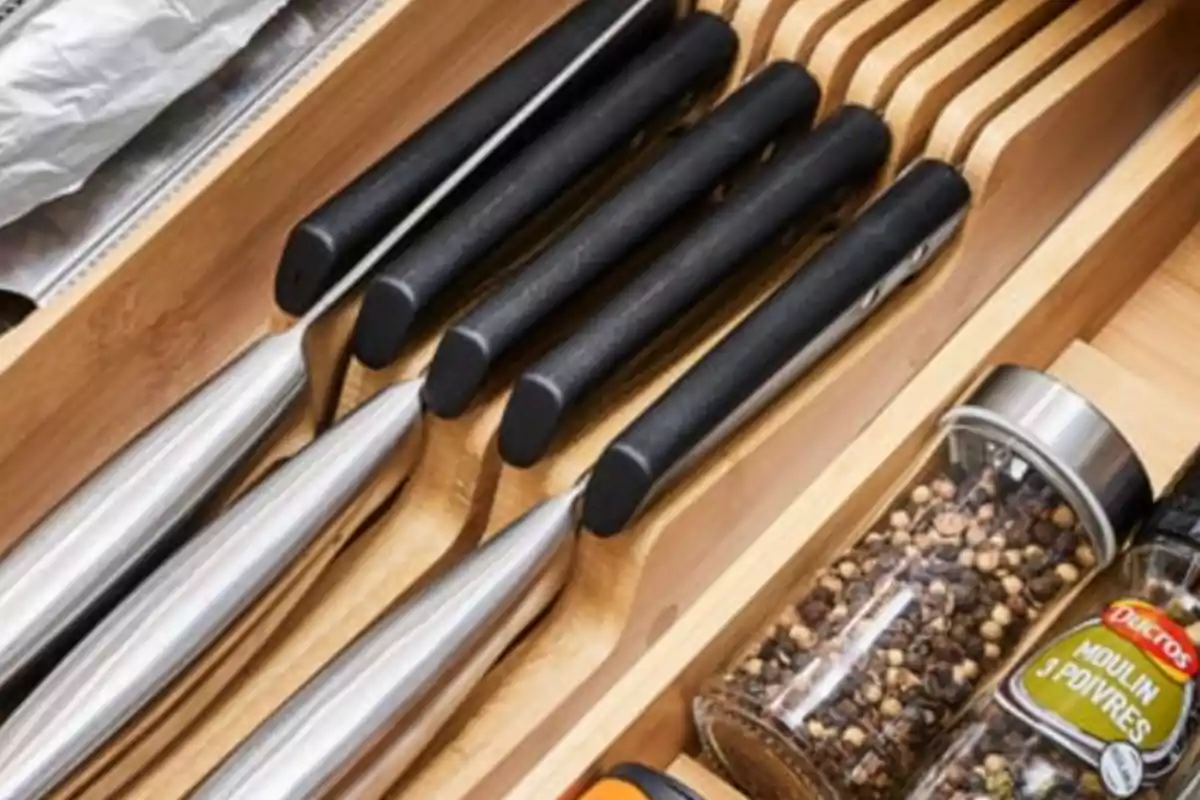 Cuchillos de cocina con mango negro organizados en un cajón de madera junto a frascos de especias