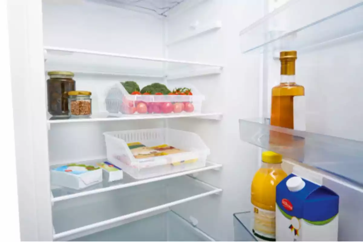 Interior de un refrigerador con algunos alimentos como verduras, frascos, jugo, leche y una botella de aceite.