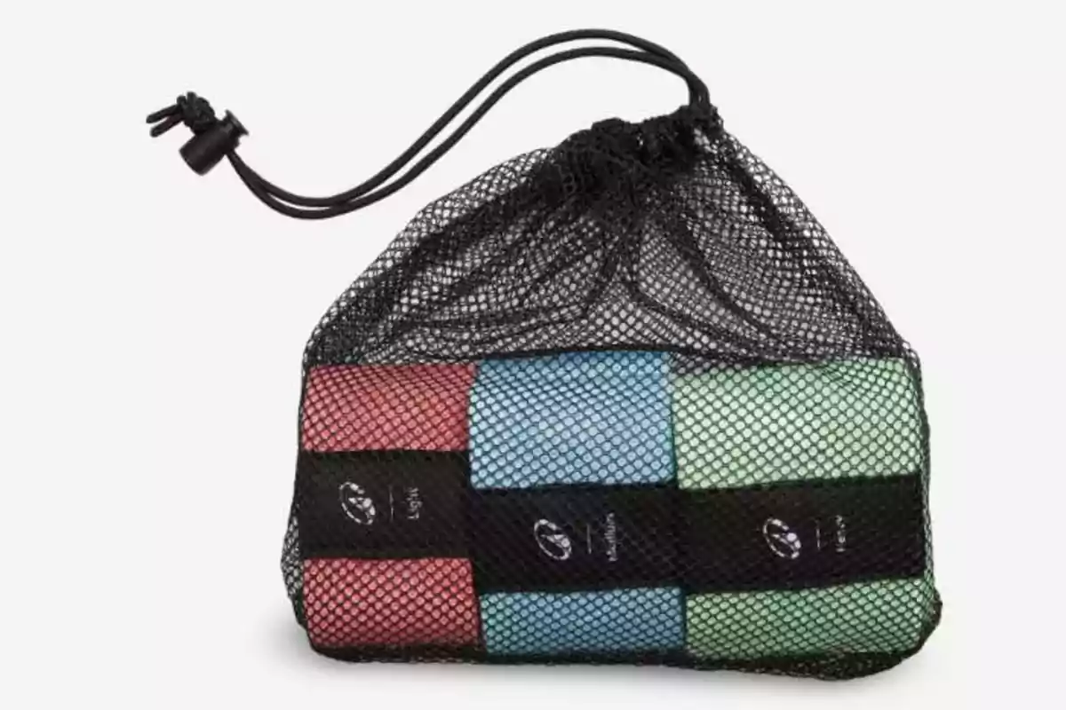 Bolsa de malla negra con cierre de cordón que contiene seis toallas enrolladas de colores rojo, azul y verde Bolsa de malla negra con cierre de cordón que contiene seis toallas enrolladas de colores rojo, azul y verde